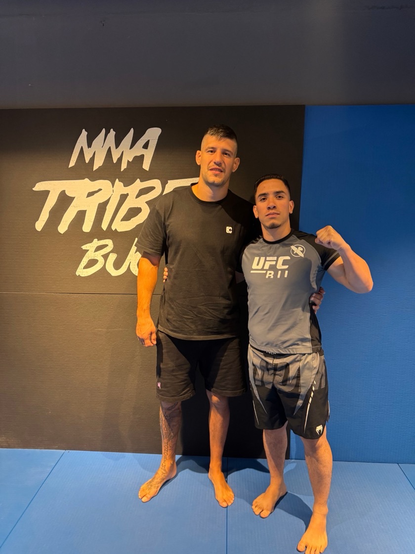 Josnier Azuaje, a la derecha, con camiseta gris y el puño en alto, junto a Joel Álvarez, peleador de la UFC, en un gimnasio de artes marciales mixtas